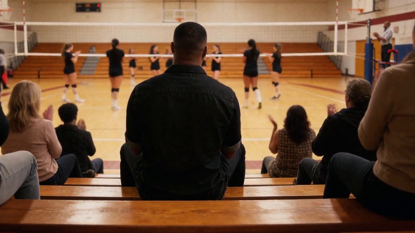 Andre in the bleachers at his daughter's volleyball game, from behind